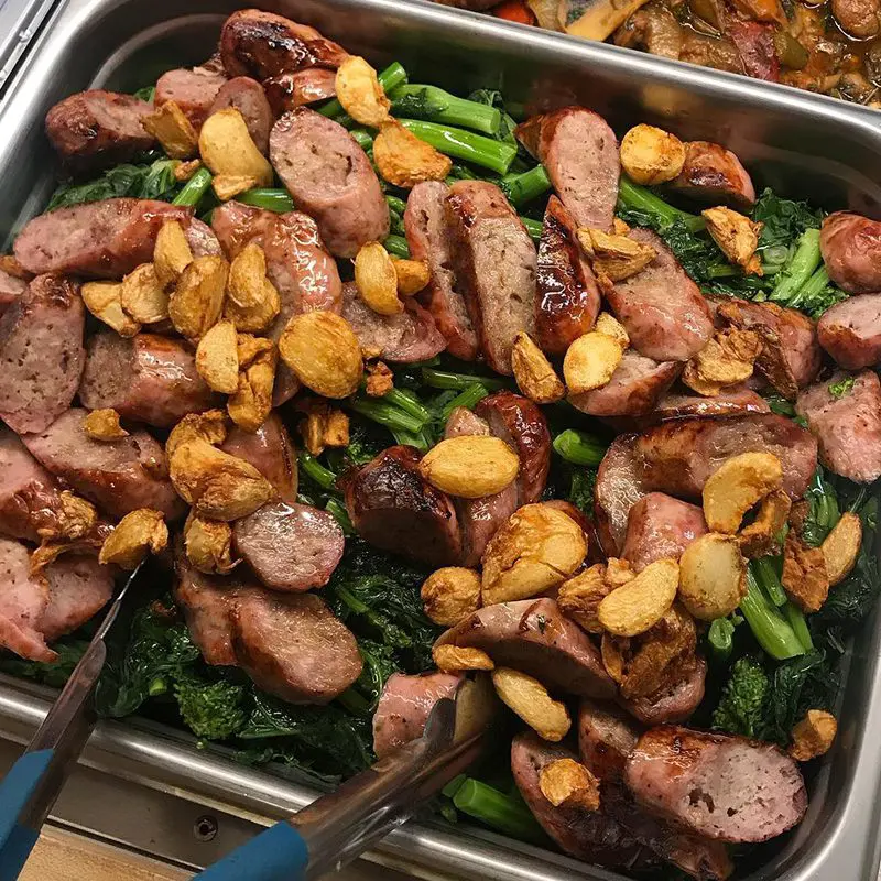 A tray of food with sausage, broccoli and potatoes.