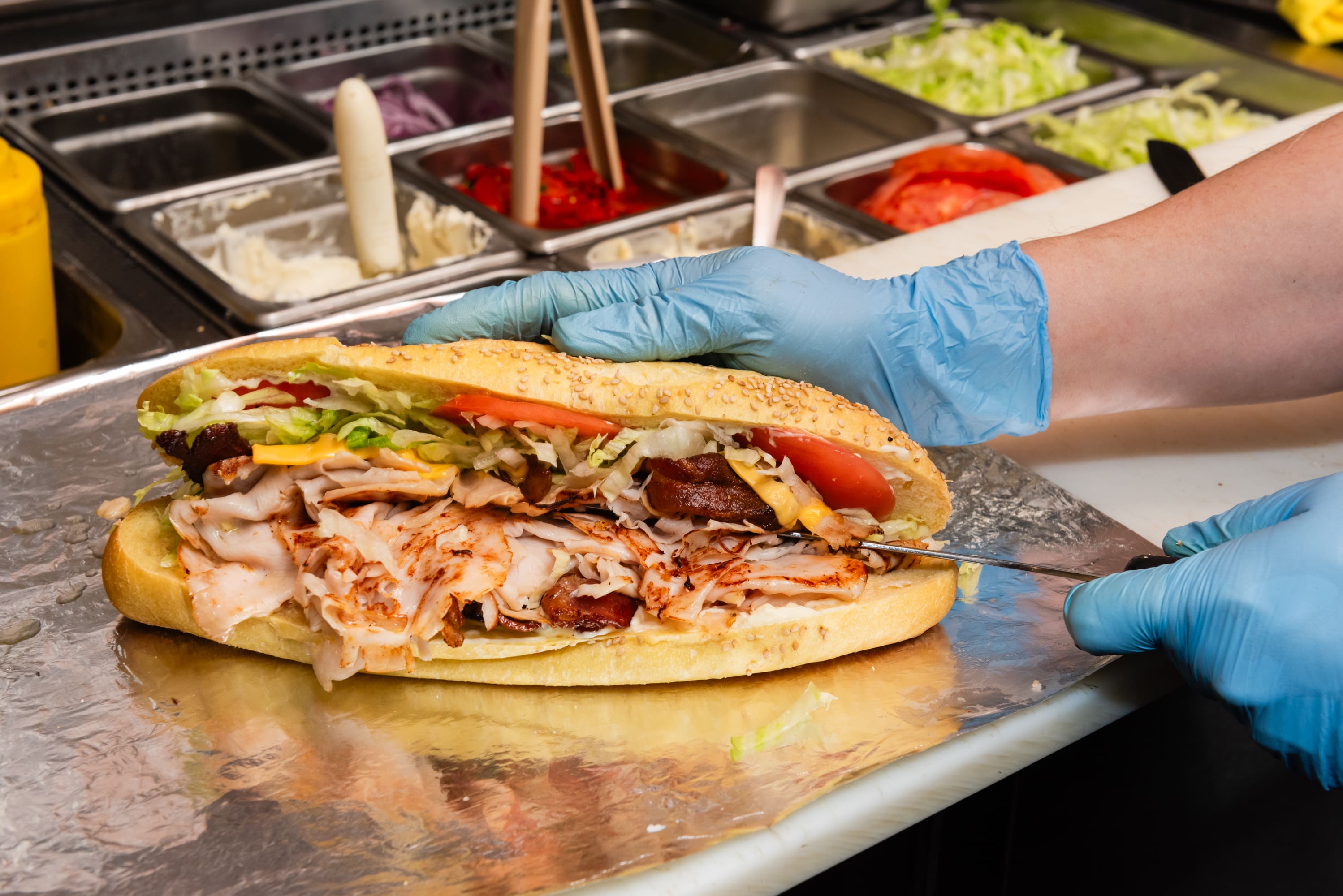 A person holding a large sandwich on top of a counter.