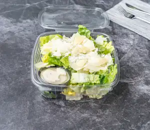 A plastic container filled with salad on top of a table.