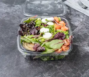 A plastic container filled with salad and dressing.