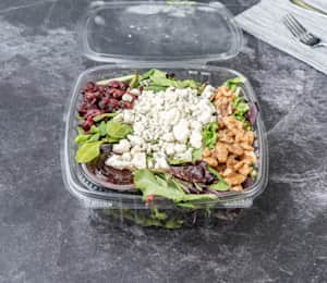 A plastic container filled with salad and nuts.